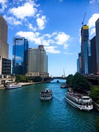 Boats in river by buildings in city against sky