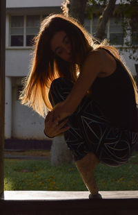 Side view of ballet dancer hugging knees while balancing with tiptoes on window sill