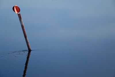 Pole against blue sky with reflection in water