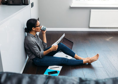 Full length businesswoman having drink while working on floor at home