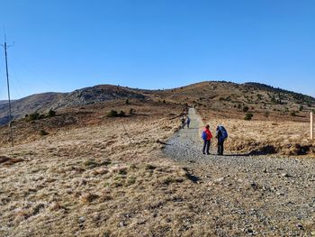 Rear view of people walking on mountain against clear blue sky