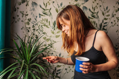 Young woman drinking water from glass wall at home