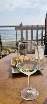 Glass of water on table by sea against sky