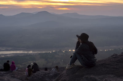 People looking at mountains against sky during sunset