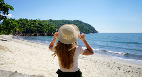 Rear view of woman standing at beach against sky