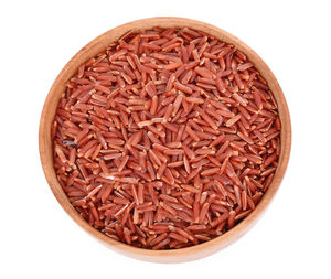 Close-up of raw brown rice in wooden container against white background