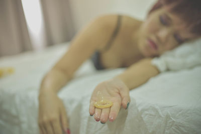Young woman holding condom while relaxing on bed at home