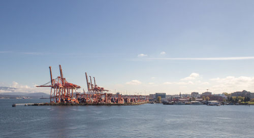 Cranes at commercial dock by sea against sky