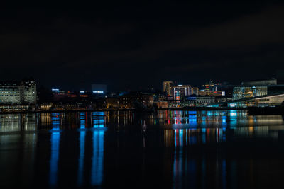 Illuminated buildings by river against sky at night