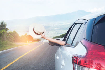 Close-up of hand holding hat in car on road against sky