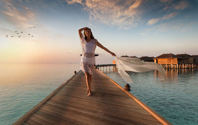 Woman standing by sea against sky during sunset