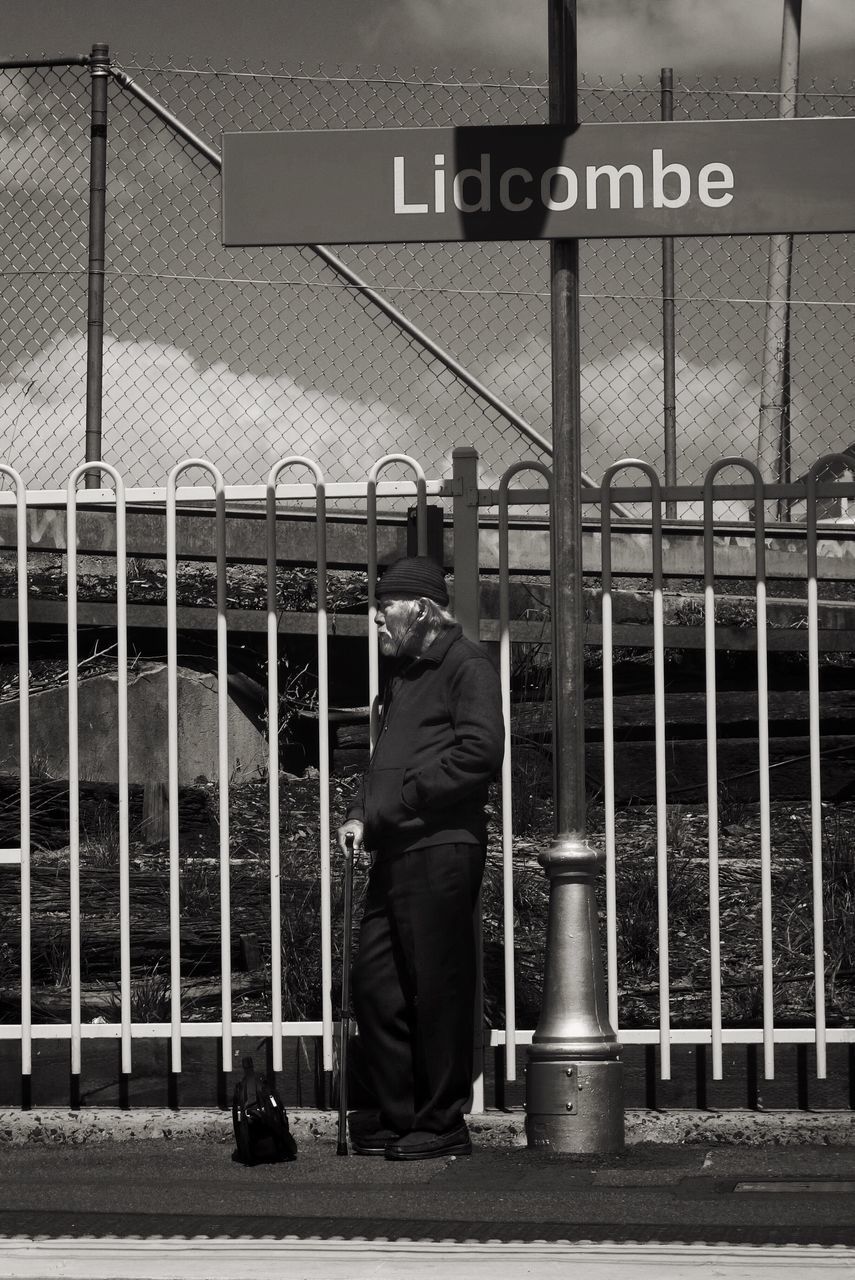 REAR VIEW OF MAN STANDING BY FENCE