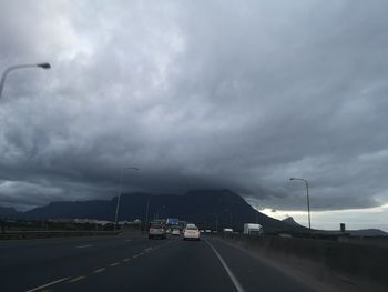 Cars on road against cloudy sky