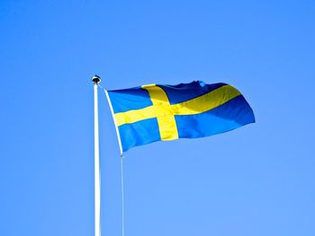 Low angle view of swedish flag waving against clear blue sky