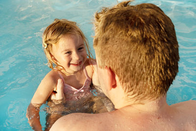High angle view of kid swimming in sea or pool with father, laughing, smiling 