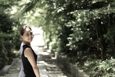 Portrait of smiling young woman standing on footpath by plants