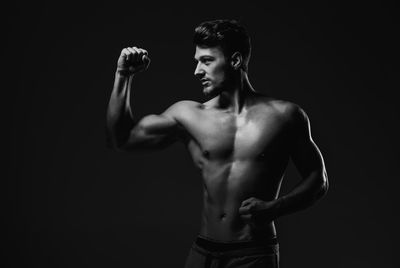 Full length of shirtless man standing against black background