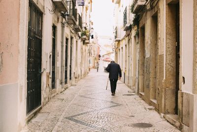 Rear view of man walking on narrow alley amidst buildings