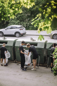 Full length of volunteers holding garbage bag with plastic by recycling bin