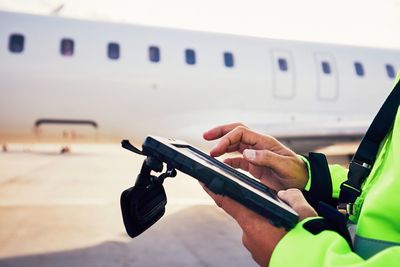 Midsection of worker using digital tablet by airplane at runway