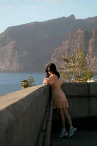 Woman standing by railing against sky