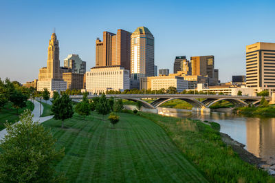 Bridge over river by buildings in city against sky