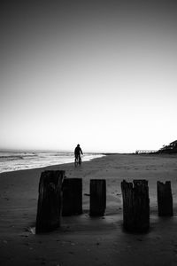 Silhouette man riding bicycle at beach against clear sky