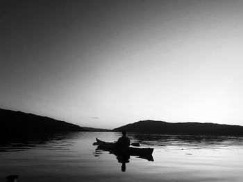 Silhouette person on lake against clear sky