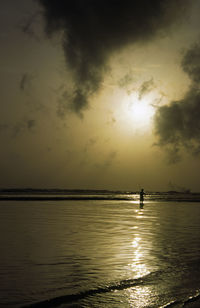 Silhouette man standing in sea against sky during sunset