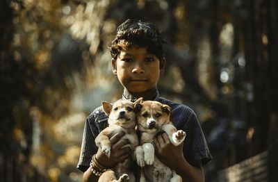 Portrait of serious boy holding puppies at public park