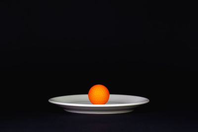 Close-up of orange slice in bowl over black background