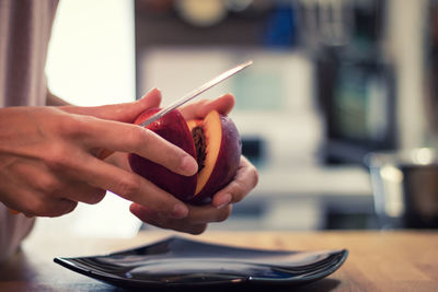 Midsection of person cutting peach in kitchen at home