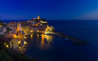Illuminated buildings by sea against clear blue sky at night