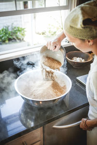 High angle view of woman mixing spices in container at kitchen counter