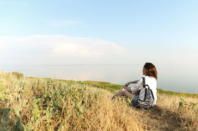 Man sitting on grass by sea against sky