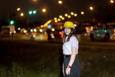 Woman standing by illuminated lights at night