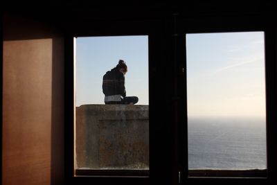 Man standing by window against sea