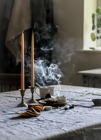 Table with linen cloth, dinner candles and tea lights blown out with wax vapour circling above.