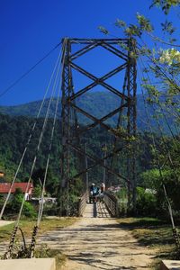 Rear view of man riding bicycle on footbridge against sky