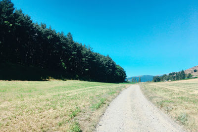 Road amidst field against clear blue sky