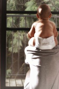 Rear view of shirtless man looking through window