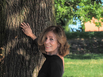 Portrait of a smiling young woman against tree trunk