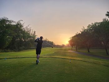 Rear view of man walking on field against sky during sunset