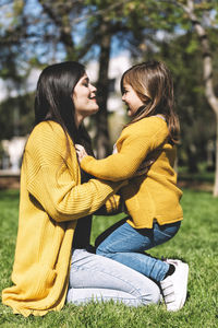 Side view of mother talking with daughter while kneeling on grassy field in park