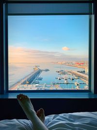 Low section of person relaxing on bed against sky seen through window