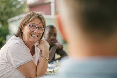 Smiling senior woman looking away while sitting at table during garden party