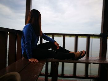 Woman sitting on bench in balcony against lake