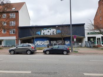 Cars on road by buildings against sky in city