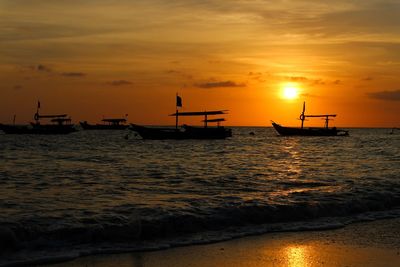 Silhouette nautical vessel on sea against orange sky