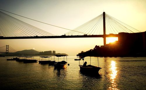 Silhouette boats moored on river by cable-stayed bridge against clear sky during sunset